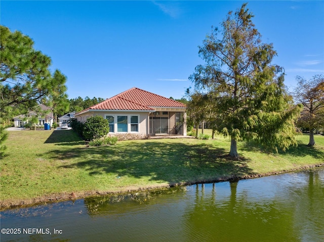 back of property with a sunroom, a yard, and a water view