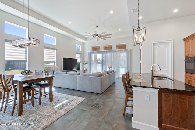 interior space featuring sink, hanging light fixtures, dark stone countertops, black oven, and ceiling fan with notable chandelier