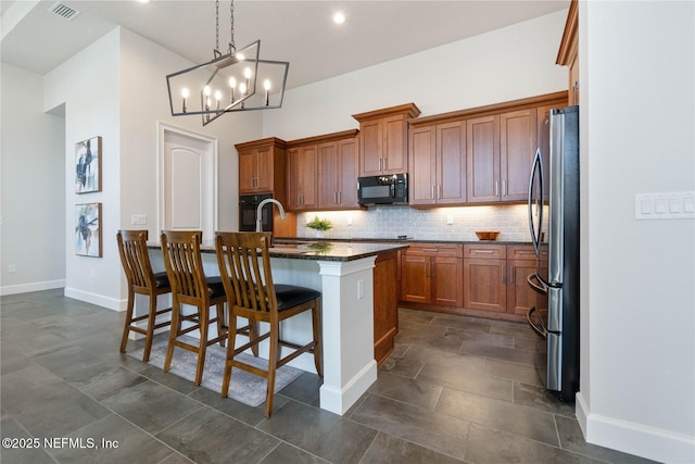 kitchen with decorative backsplash, stainless steel fridge, a kitchen breakfast bar, a kitchen island with sink, and hanging light fixtures