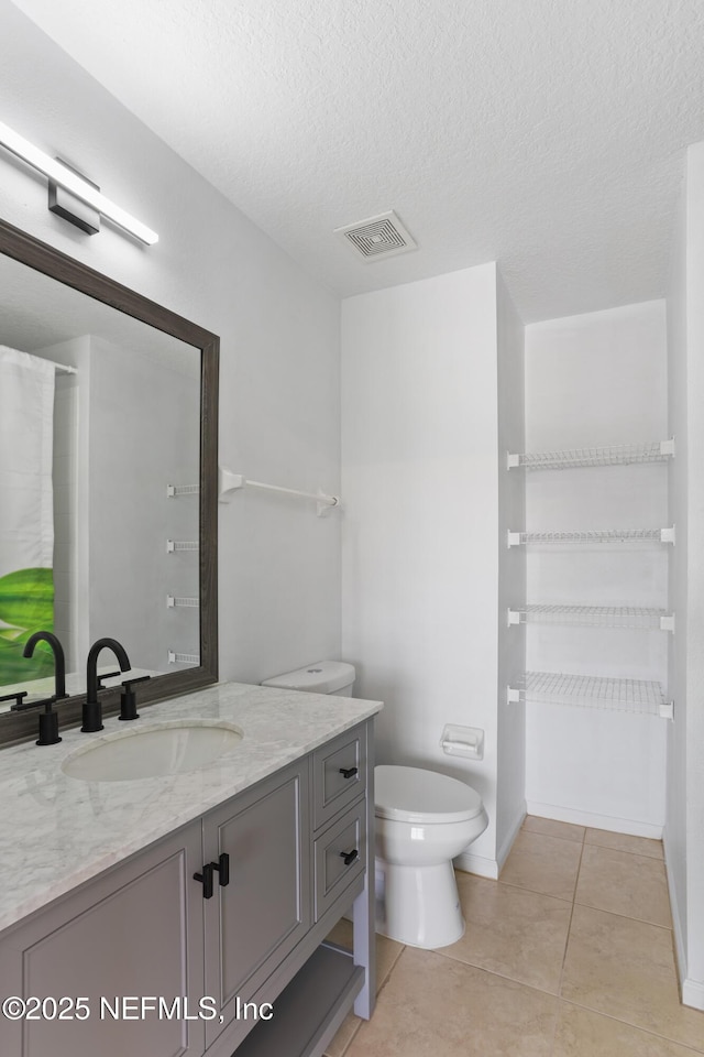 bathroom featuring tile patterned flooring, a textured ceiling, vanity, and toilet