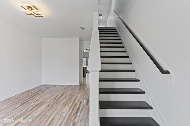 staircase with wood-type flooring and a textured ceiling