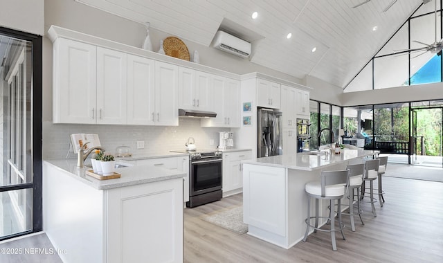 kitchen with stainless steel appliances, high vaulted ceiling, white cabinetry, a wall mounted air conditioner, and sink