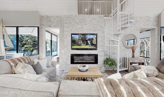 living room featuring a high ceiling, a wealth of natural light, hardwood / wood-style flooring, and a stone fireplace