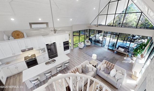 living room with high vaulted ceiling, ceiling fan, light wood-type flooring, and sink