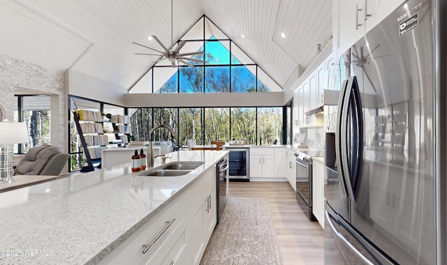 kitchen featuring beverage cooler, appliances with stainless steel finishes, light stone counters, white cabinets, and sink