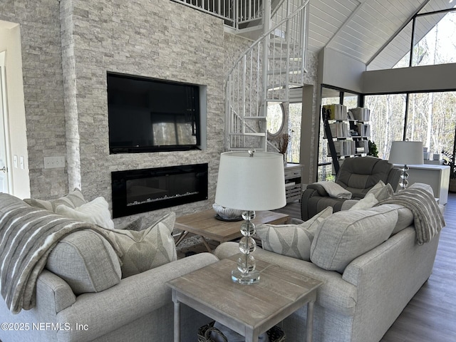 living room featuring high vaulted ceiling, hardwood / wood-style floors, beamed ceiling, and a stone fireplace