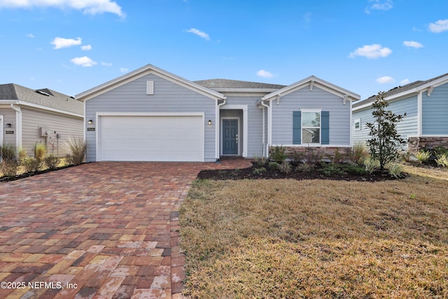 single story home with an attached garage, stone siding, decorative driveway, and a front yard