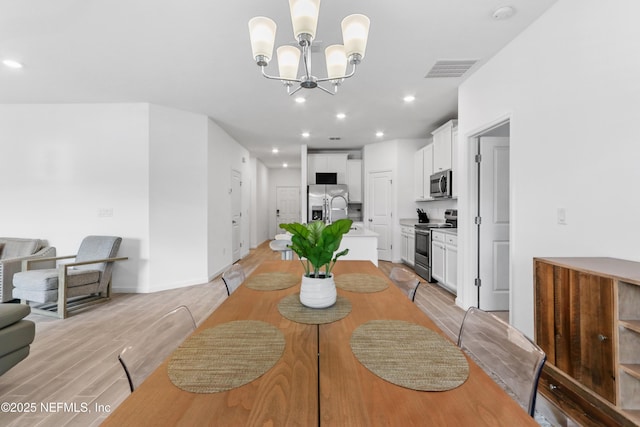 dining space featuring light wood finished floors, recessed lighting, visible vents, an inviting chandelier, and baseboards