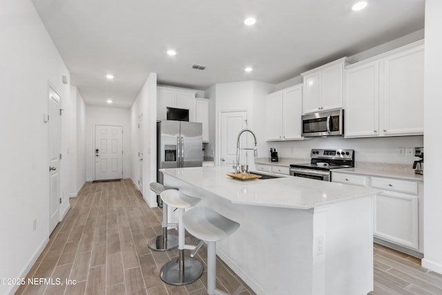 kitchen with a center island with sink, light stone countertops, white cabinetry, and appliances with stainless steel finishes