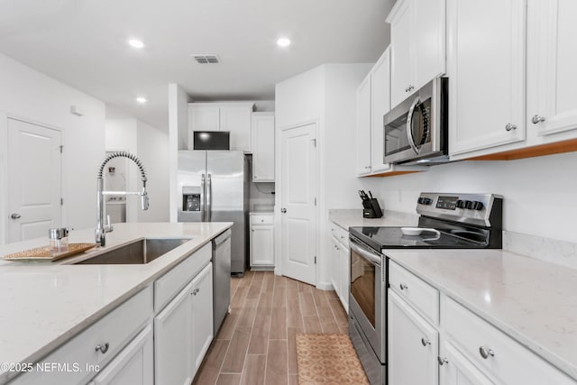 kitchen with light stone counters, stainless steel appliances, visible vents, white cabinetry, and wood tiled floor