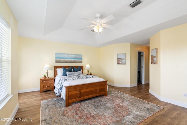 bedroom with a tray ceiling, wood-type flooring, and ceiling fan