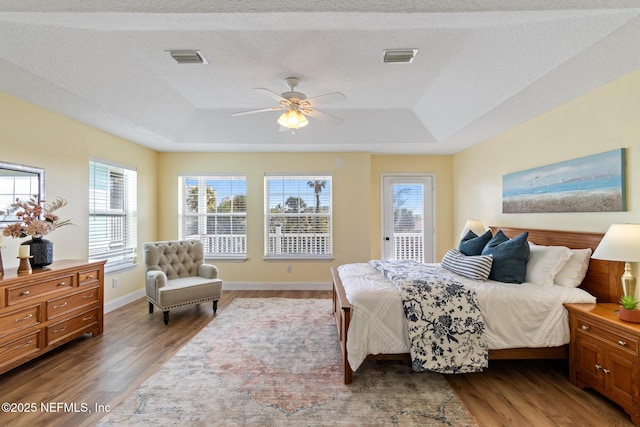 bedroom featuring a raised ceiling, dark hardwood / wood-style floors, and multiple windows