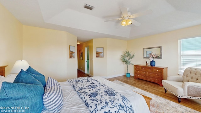 bedroom with ceiling fan, light wood-type flooring, and a tray ceiling