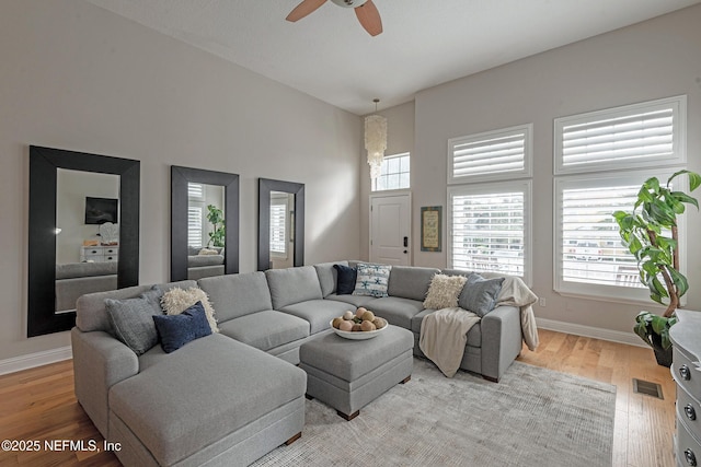 living room with ceiling fan, light hardwood / wood-style flooring, and a high ceiling