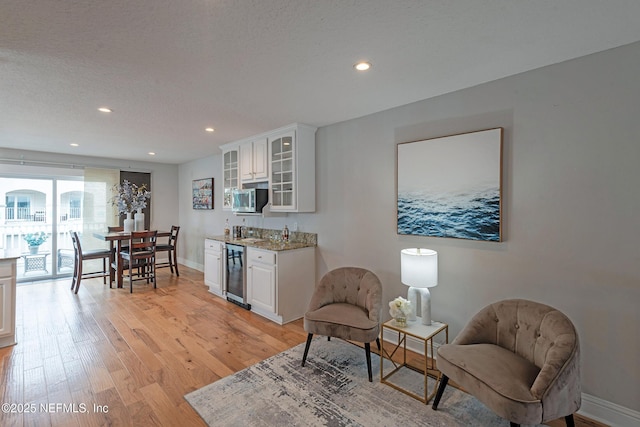 interior space featuring bar area, beverage cooler, a textured ceiling, and light wood-type flooring