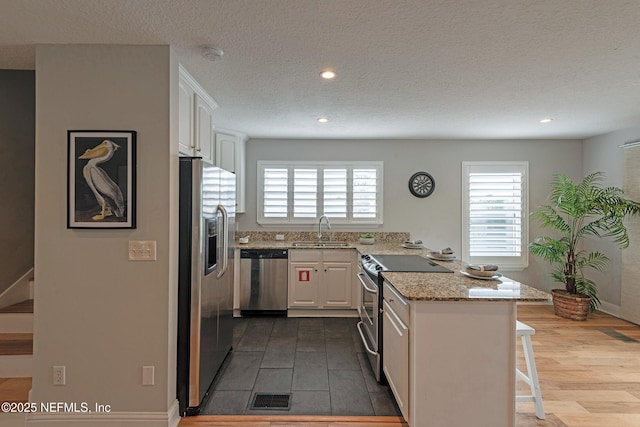 kitchen featuring a kitchen breakfast bar, sink, light stone countertops, appliances with stainless steel finishes, and white cabinetry