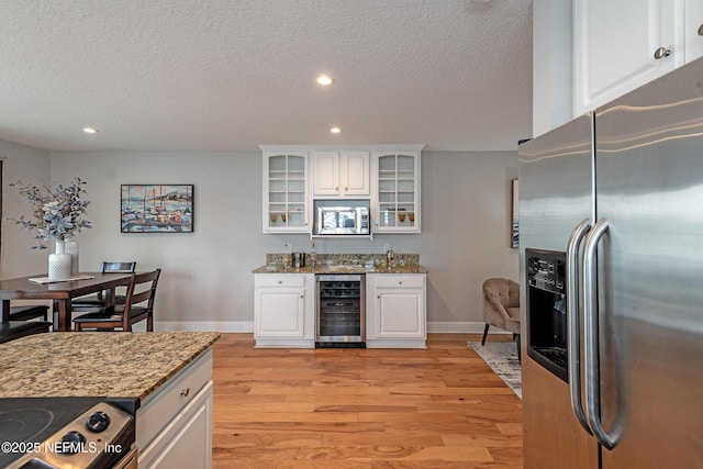 kitchen featuring white cabinets, appliances with stainless steel finishes, light hardwood / wood-style floors, light stone counters, and beverage cooler