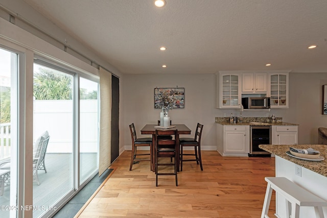 dining area with bar area, beverage cooler, a textured ceiling, and light hardwood / wood-style flooring