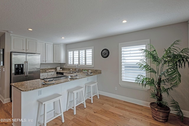 kitchen featuring white cabinetry, kitchen peninsula, stainless steel fridge, and dark stone countertops