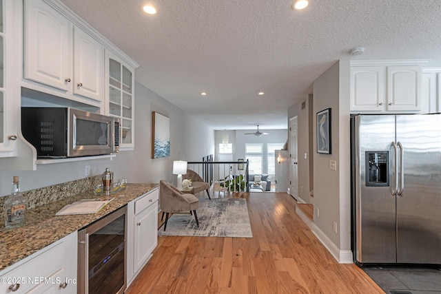 kitchen with dark stone counters, stainless steel appliances, beverage cooler, ceiling fan, and white cabinetry