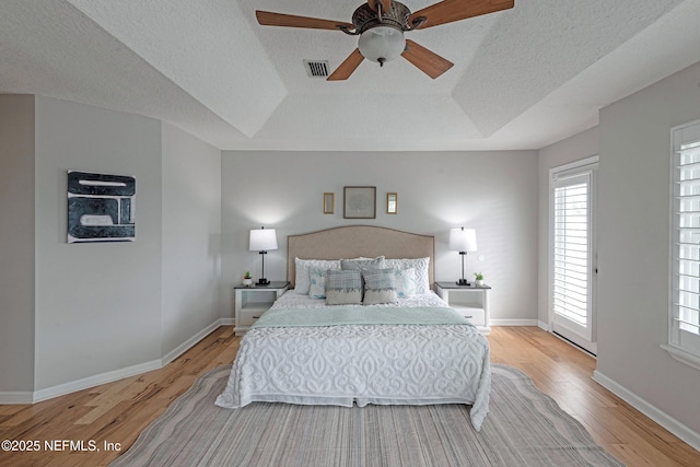 bedroom featuring ceiling fan, light hardwood / wood-style floors, a raised ceiling, and a textured ceiling