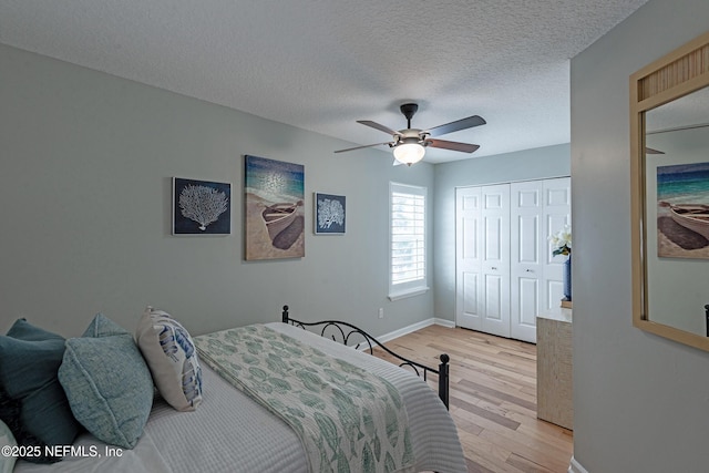 bedroom with a textured ceiling, a closet, light hardwood / wood-style floors, and ceiling fan