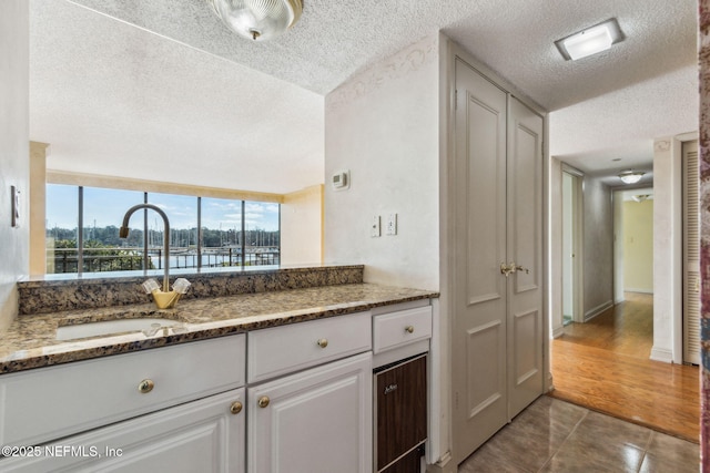 kitchen with sink, white cabinetry, dark stone countertops, a textured ceiling, and tile patterned floors