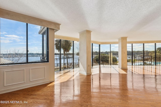 interior space featuring light hardwood / wood-style floors, ornate columns, a textured ceiling, and a water view