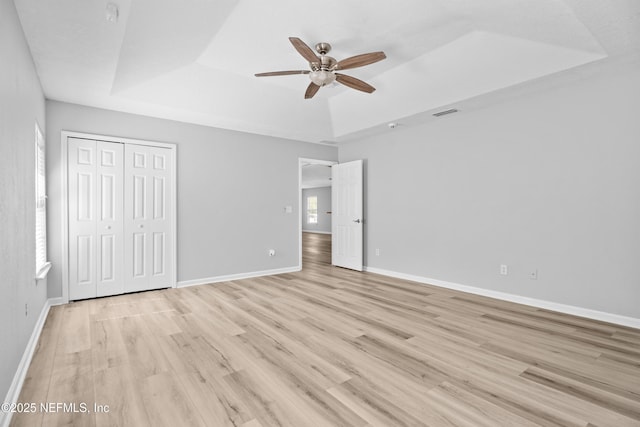 unfurnished bedroom with a raised ceiling, ceiling fan, light hardwood / wood-style floors, and a closet