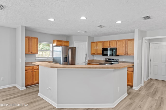 kitchen featuring stainless steel appliances, an island with sink, light wood-type flooring, a textured ceiling, and sink