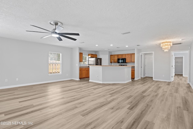 unfurnished living room featuring ceiling fan with notable chandelier, light wood-type flooring, and a textured ceiling