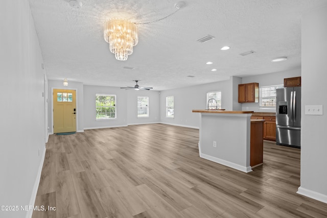 unfurnished living room featuring a textured ceiling, light wood-type flooring, and ceiling fan with notable chandelier