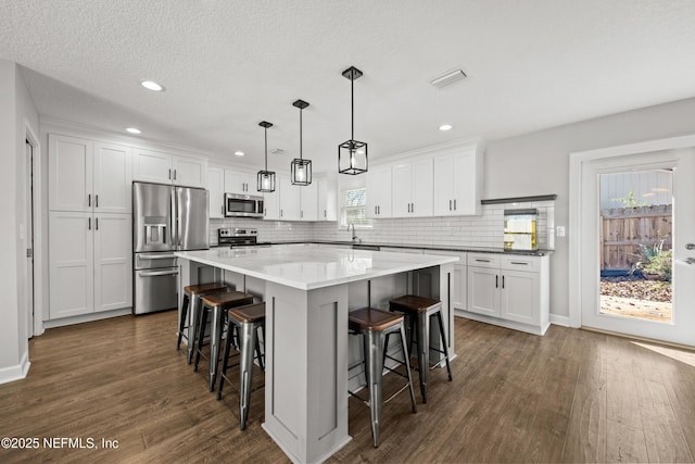 kitchen with appliances with stainless steel finishes, a breakfast bar, decorative light fixtures, white cabinets, and a kitchen island