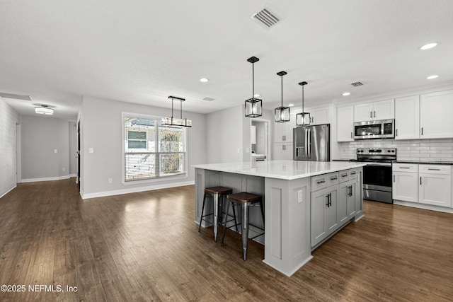 kitchen with backsplash, hanging light fixtures, appliances with stainless steel finishes, a kitchen island, and white cabinetry