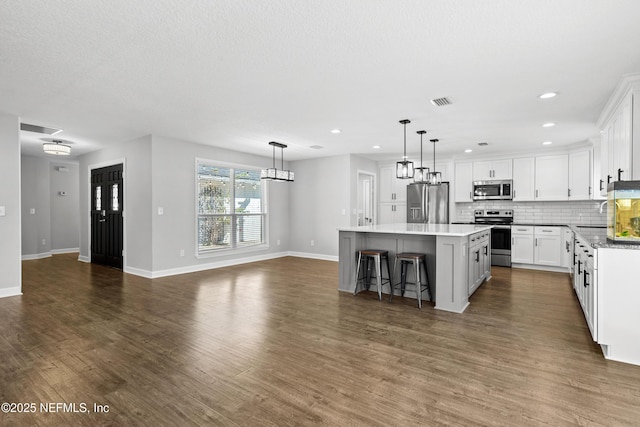 kitchen featuring white cabinetry, stainless steel appliances, pendant lighting, a breakfast bar area, and a kitchen island