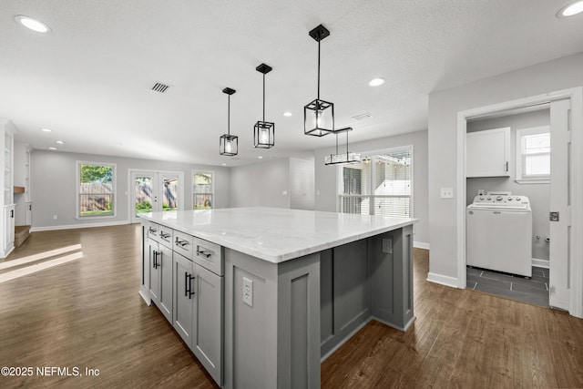 kitchen featuring a center island, light stone countertops, decorative light fixtures, dark hardwood / wood-style flooring, and washer / clothes dryer