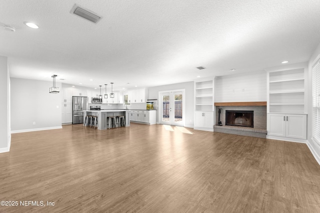 unfurnished living room featuring light hardwood / wood-style flooring, a textured ceiling, and a brick fireplace