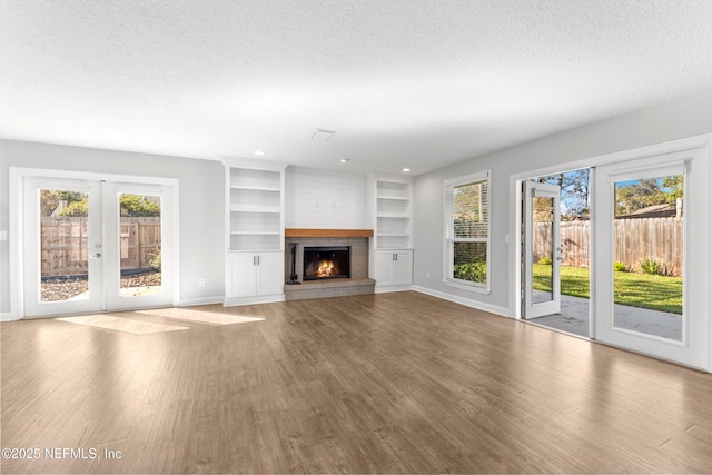 unfurnished living room featuring french doors, light hardwood / wood-style flooring, built in shelves, a textured ceiling, and a fireplace