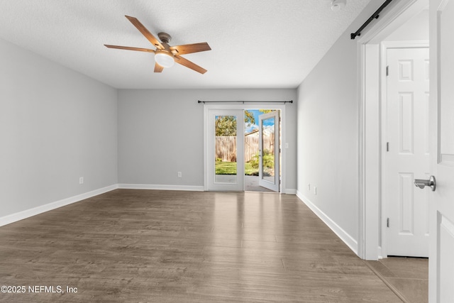 spare room with a barn door, ceiling fan, dark wood-type flooring, and a textured ceiling