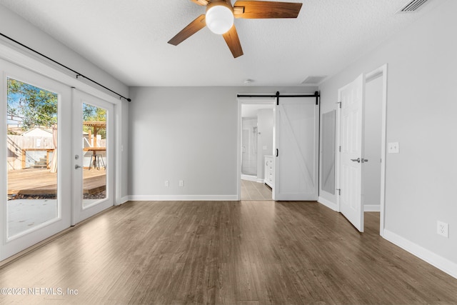 unfurnished room with a textured ceiling, ceiling fan, a barn door, and dark wood-type flooring