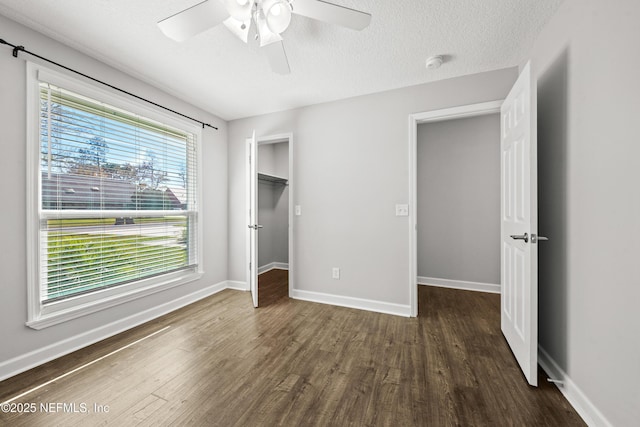 unfurnished bedroom with a walk in closet, ceiling fan, dark hardwood / wood-style floors, a textured ceiling, and a closet