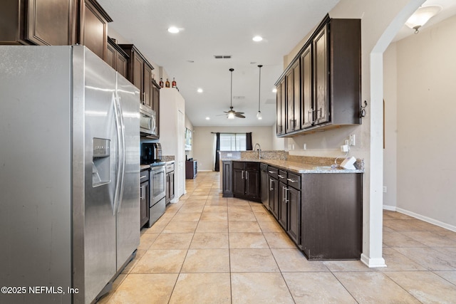 kitchen with light stone countertops, appliances with stainless steel finishes, dark brown cabinets, ceiling fan, and hanging light fixtures