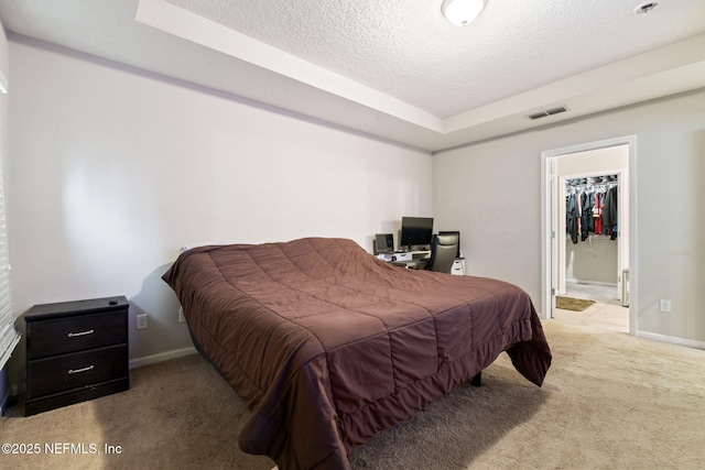 carpeted bedroom featuring a closet, a spacious closet, a textured ceiling, and a tray ceiling