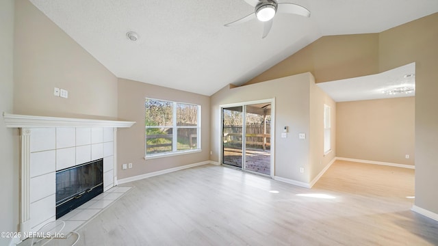 unfurnished living room with a tiled fireplace, ceiling fan, light hardwood / wood-style flooring, and lofted ceiling