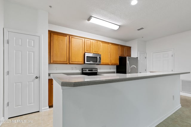 kitchen with a textured ceiling, light tile patterned flooring, stainless steel appliances, and an island with sink