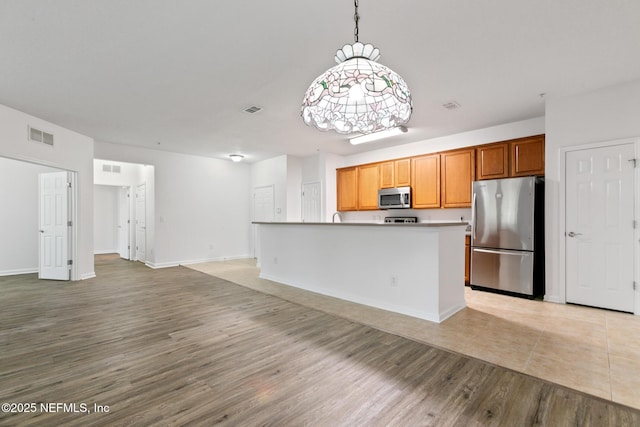 kitchen with a center island, stainless steel appliances, an inviting chandelier, pendant lighting, and light hardwood / wood-style floors