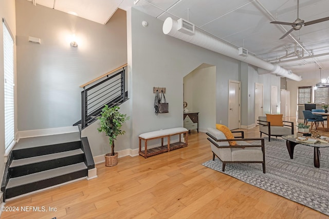 living room with a towering ceiling, light wood-type flooring, and ceiling fan