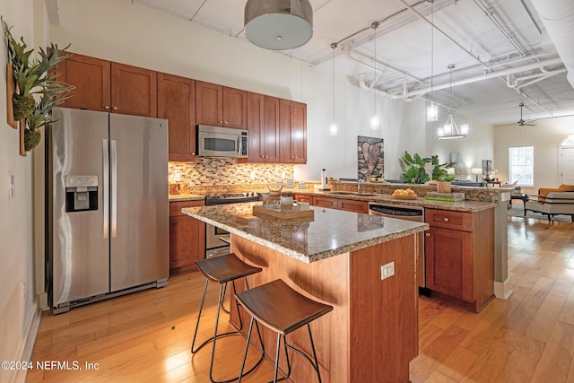 kitchen featuring kitchen peninsula, appliances with stainless steel finishes, a kitchen breakfast bar, a center island, and hanging light fixtures