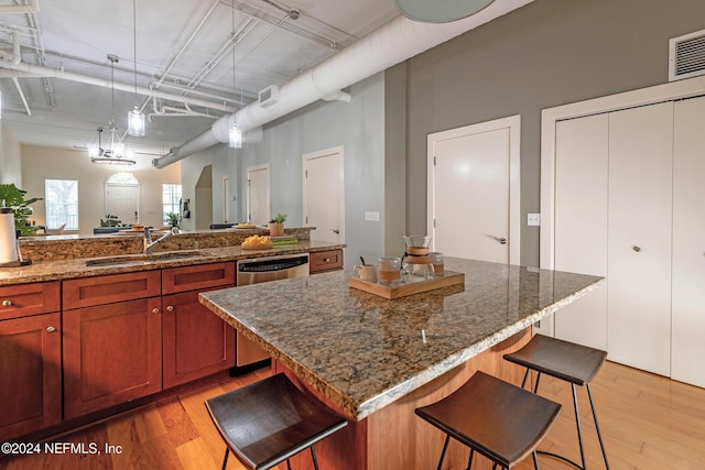 kitchen featuring sink, stainless steel dishwasher, decorative light fixtures, a kitchen island, and a breakfast bar area