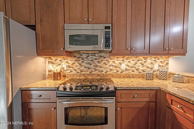 kitchen with tasteful backsplash, light stone counters, and appliances with stainless steel finishes